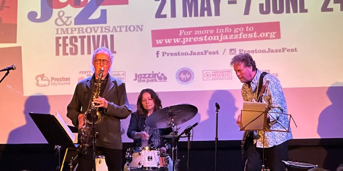 A jazz band playing on a stage with the Preston Jazz Festival logo displayed behind them