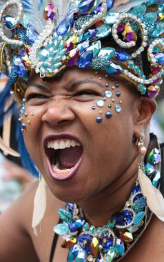 Woman in 2017 Preston Caribbean Carnival parade roaring for camera, wearing blue jewelled headdress.