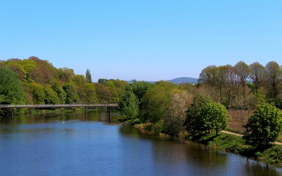 View of River Ribble from bridge on sunny day with hills and view of Preston in the background.