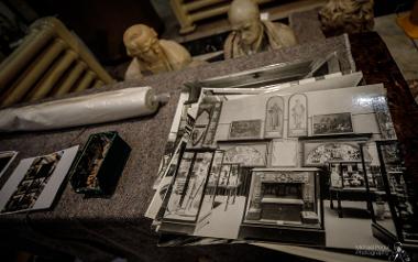 Numerous black and white old photos of The Harris on table, with packing items and busts in background.