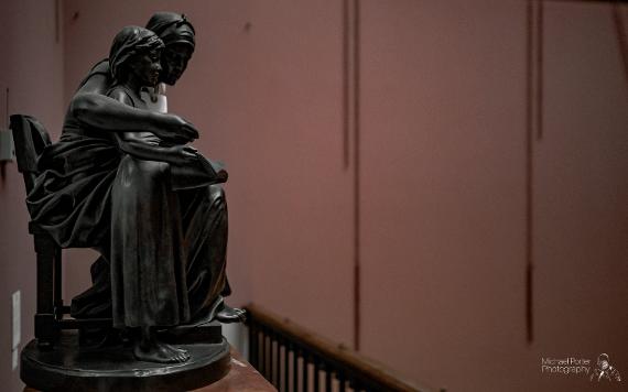 Statue of mother and child with empty red walls in background.