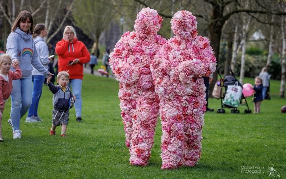 Two people dressed in costumes made of flowers walking through Avenham Park