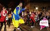 A man in a yellow and blue outfit and backup dancers dancing in the torchlight procession in Preston