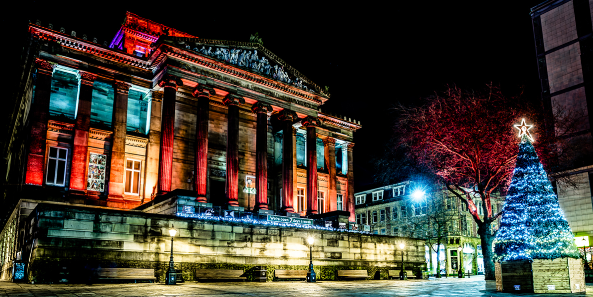 A night photo of the front of The Harris building lit up with colourful lights and a Christmas tree with colourful lights