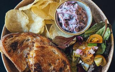 A plate of a grilled cheese sandwich, crisps, salad and coleslaw from Brew + Bake