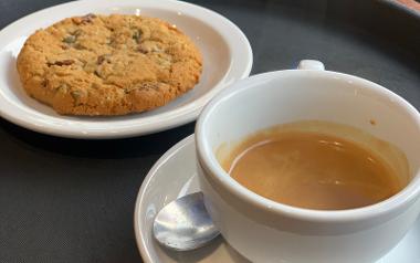 A close up of a cup of coffee and a chocolate chip cookie from Caffé Nero