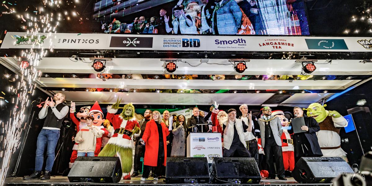 A group of performers and singers and guests on a stage after turning on Preston City Centre's Christmas Lights