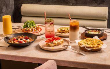 A variety of plates with brunch menu items on them, including Shakshuka, Keralan Spiced Beans on Sourdough, and their Signature Chai and Pecan Granola