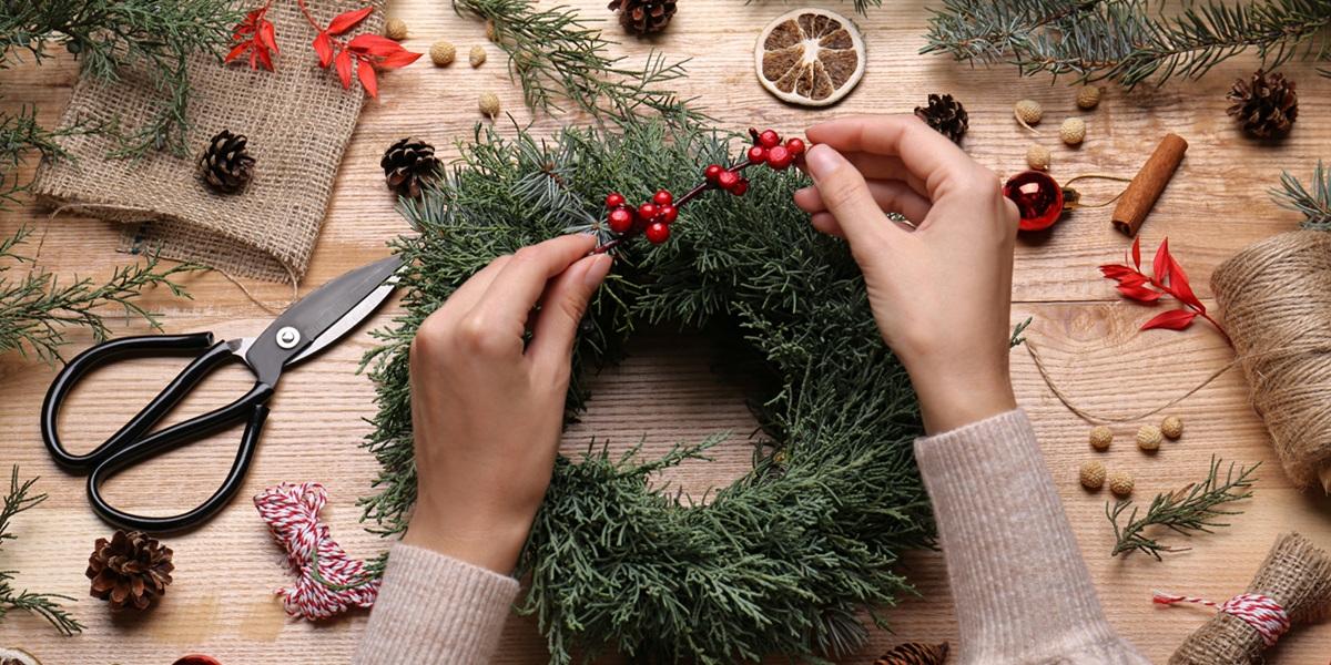 Florist making beautiful Christmas wreath with berries on wooden table, top view.