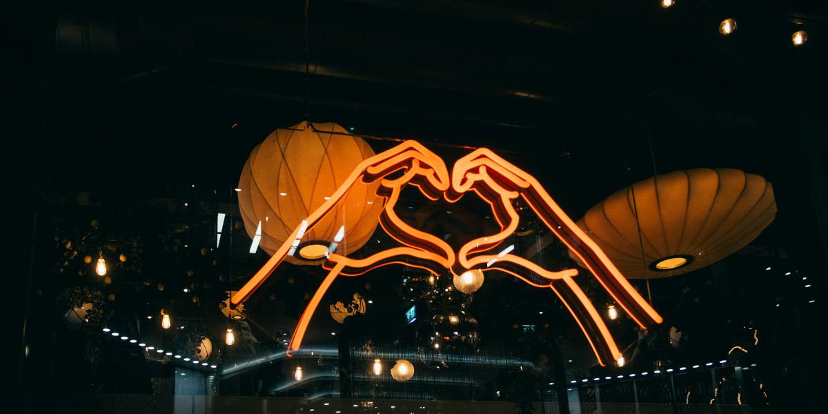 A neon sign in the window of Ask Italian showing hands folded into a heart symbol