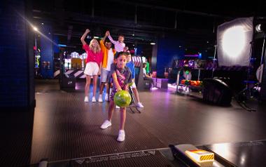 A girl throwing a bowling ball while her family cheers behind her