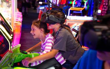 Two kids wearing virtual reality headsets while riding arcade motorcycles