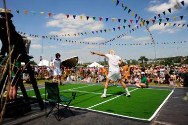 Two people playing tennis on a small court to a crowd of people