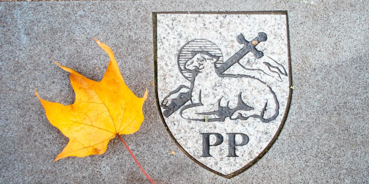 Main image: Preston Lamb coat of arms carved in stone with an autumn leaf next to it. Preston Lamb coat of arms carved in stone with an autumn leaf next to it.