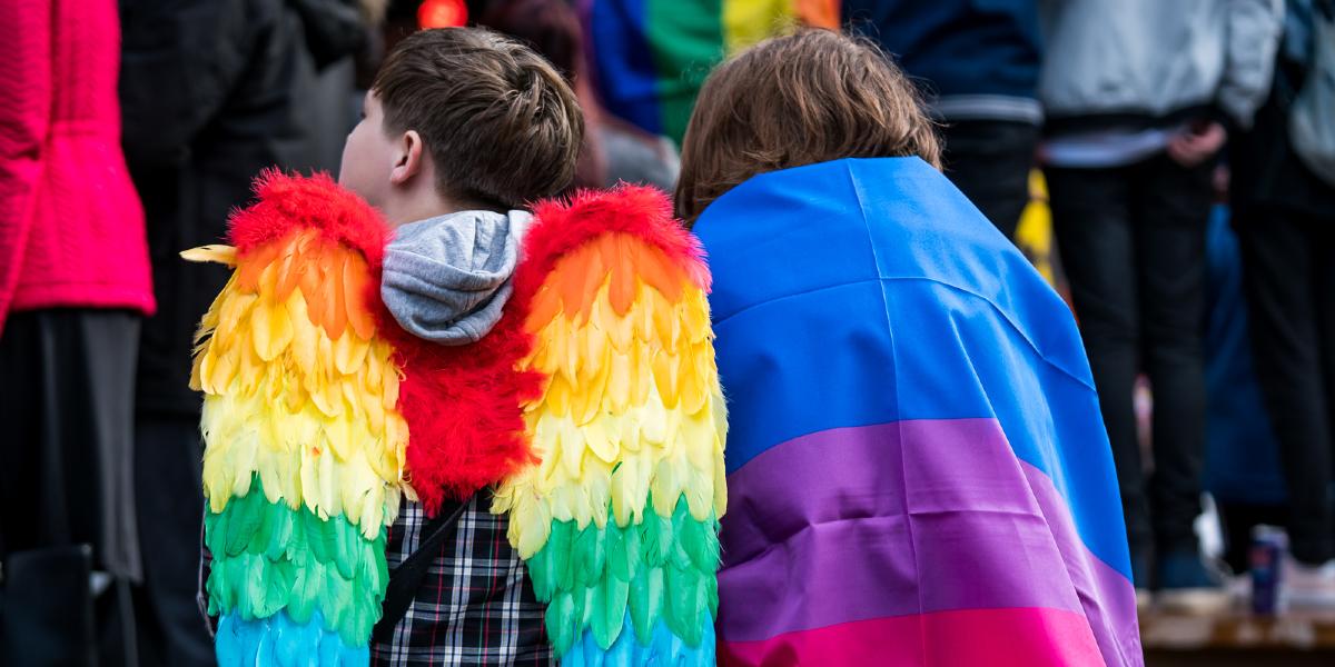 Main image: Boy with rainbow fairy wings and girl draped in a pride flag. Boy with rainbow fairy wings and girl draped in a pride flag.