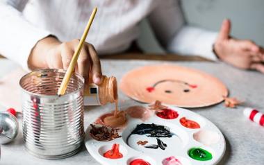 Young girl painting a smiley face on a paper plate.