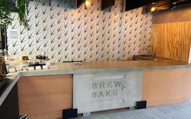 A serving counter with a selection of cakes and the logo of Brew + Bake café