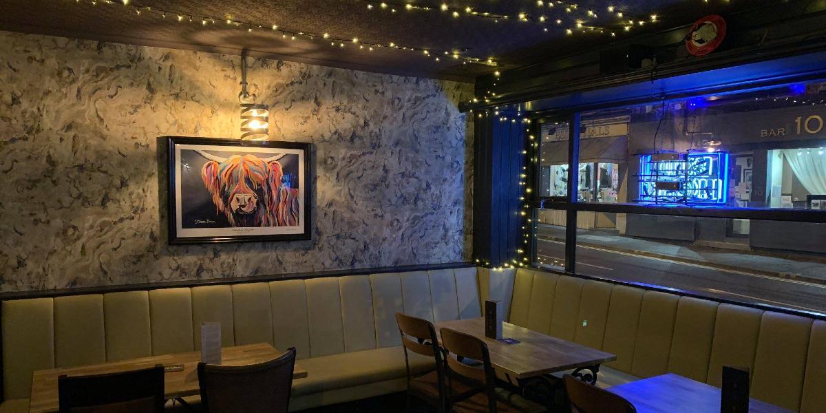Main image: Bench seating and tables inside The Angel, with fairy lights and artwork on walls. Bench seating and tables inside The Angel, with fairy lights and artwork on walls.