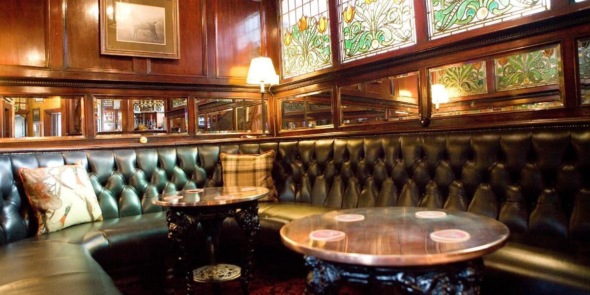 Green leather corner seating and wooden panelled walls inside The Black Horse pub, Preston.