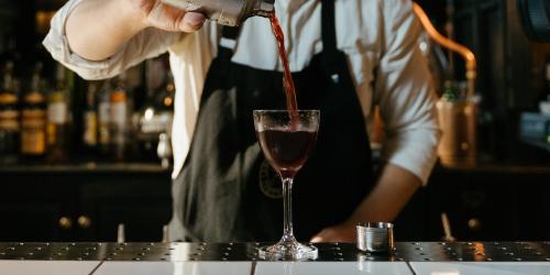 Page icon: Bartender pouring red cocktail into glass at bar. Bartender pouring red cocktail into glass at bar.