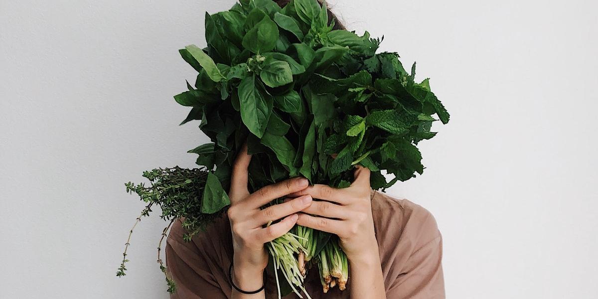 Main image Preston Vegan Society Woman hiding her face with bunch of spinach and herbs.