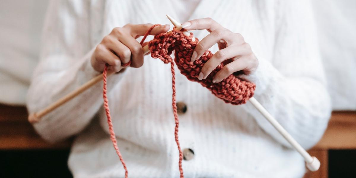 Main image: Woman sat knitting. Woman sat knitting with orange wool.